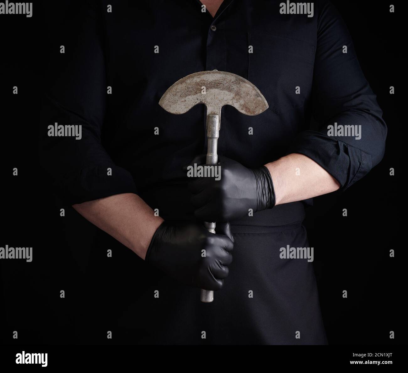 hombre con ropa negra, guantes de látex sostiene un cuchillo de hacha de metal vintage para carne y verduras Foto de stock