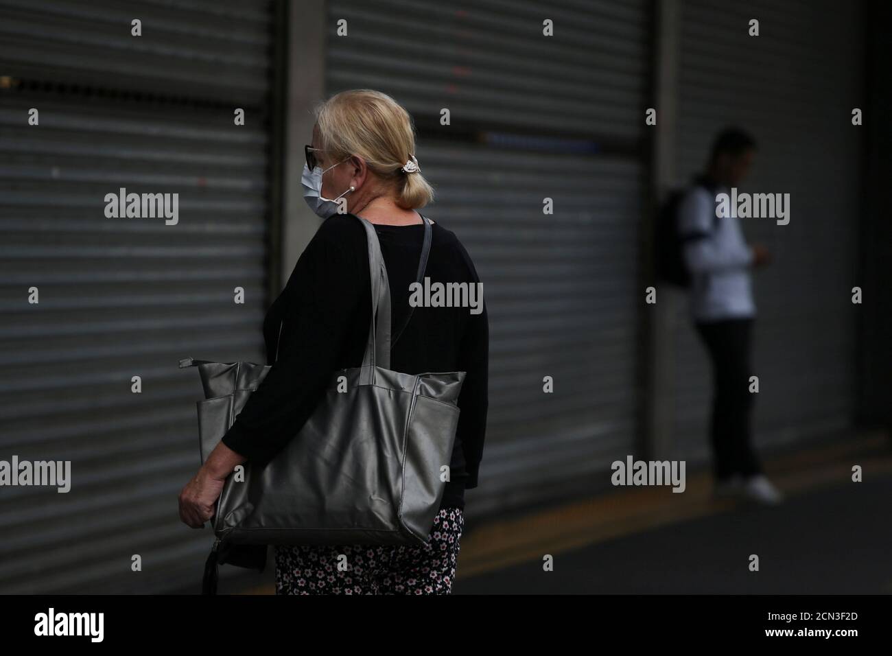 Una mujer que lleva una máscara se encuentra frente a un centro comercial cerrado que redujo sus horas de apertura en medio del brote de la enfermedad del coronavirus (COVID-19) en Sao Paulo, Brasil 19 de marzo de 2020. REUTERS/Rahel Patrasso Foto de stock