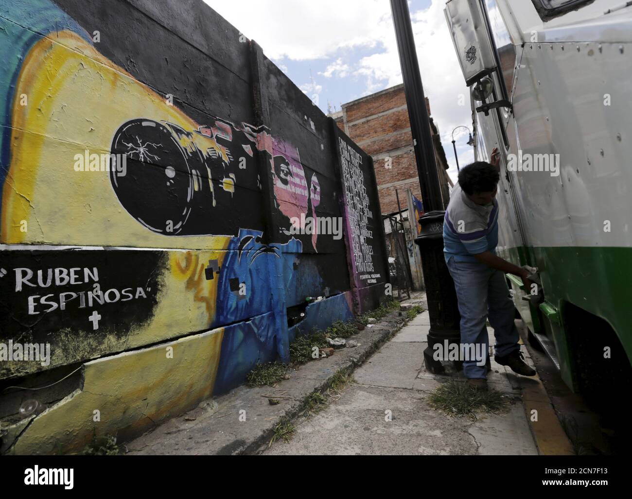 Un hombre limpia un autobús cerca de una pared con una imagen que  representa al destacado fotógrafo de noticias mexicano Rubén Espinosa,  quien fue asesinado junto con otras cuatro mujeres, a lo