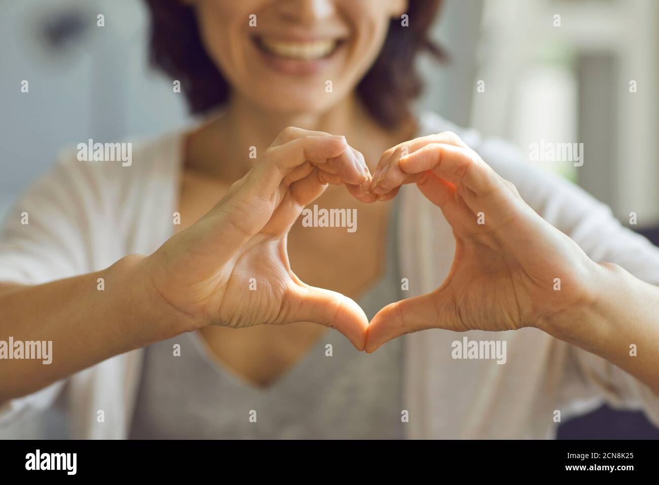 Imagen de enfoque superficial recortada de una mujer sonriente feliz mostrando el corazón símbolo con sus manos Foto de stock