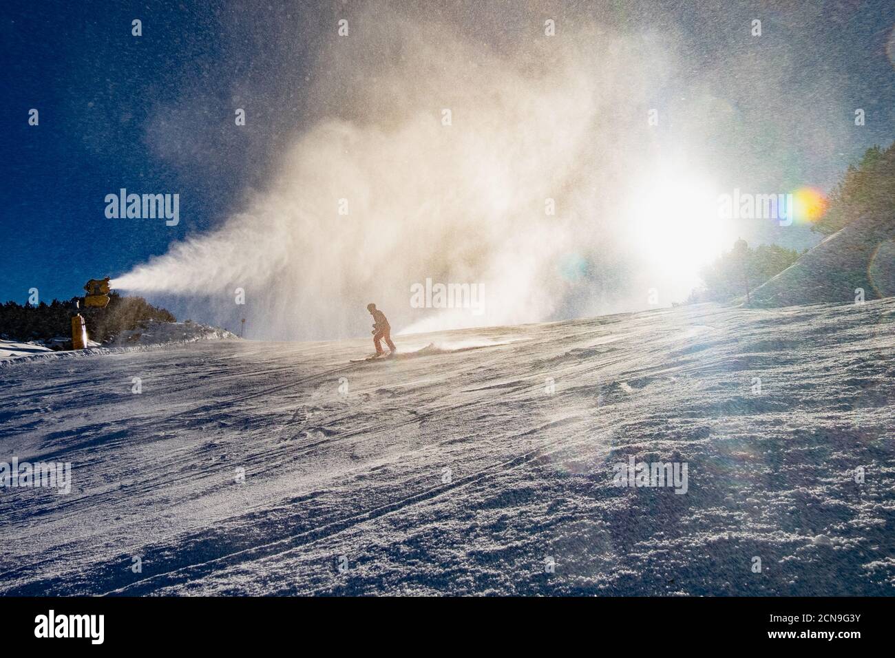Gente esquiando abajo de canon de nieve en funcionamiento Foto de stock