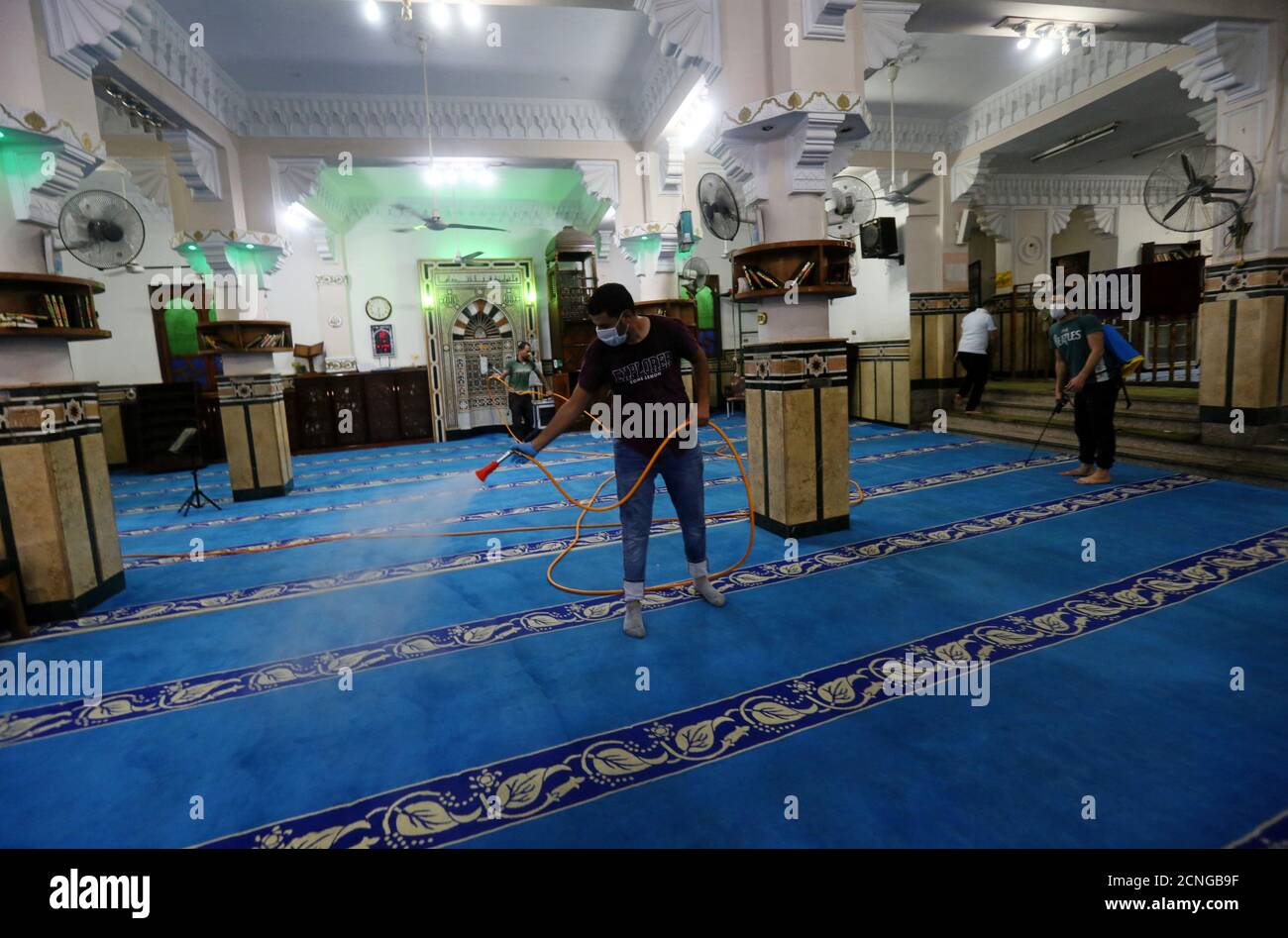 Los voluntarios que usan mascarillas pulverizan desinfectante dentro de una mezquita, ya que está preparada para la oración después de ser reabierta, después del brote de la enfermedad coronavirus (COVID-19), en el Cairo, Egipto, 26 de junio de 2020. REUTERS/Mohamed Abd el Ghany Foto de stock