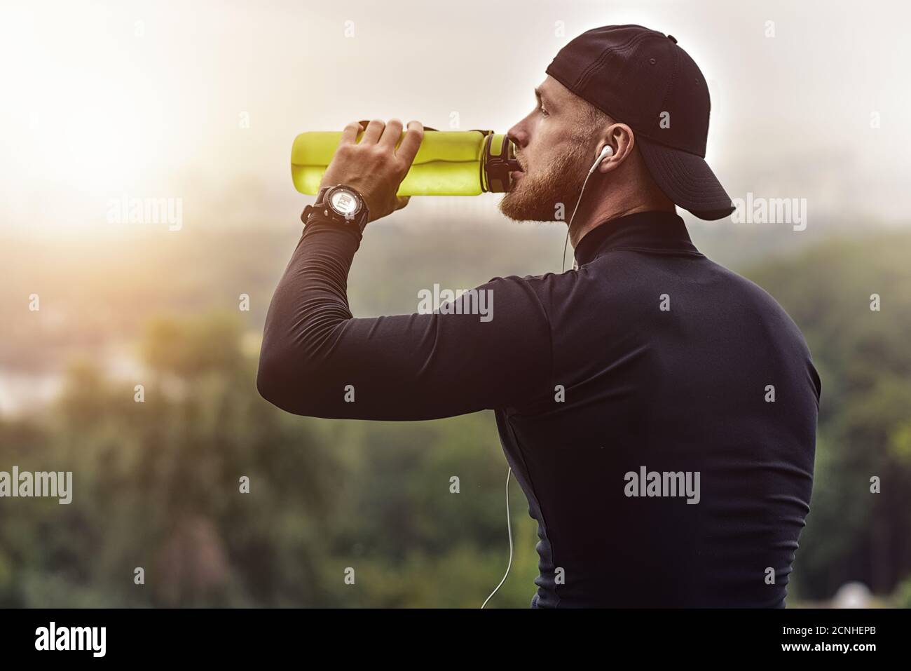 Musculoso atleta barbado beber agua después de una buena sesión de entrenamiento en el parque de la ciudad. Foto de stock