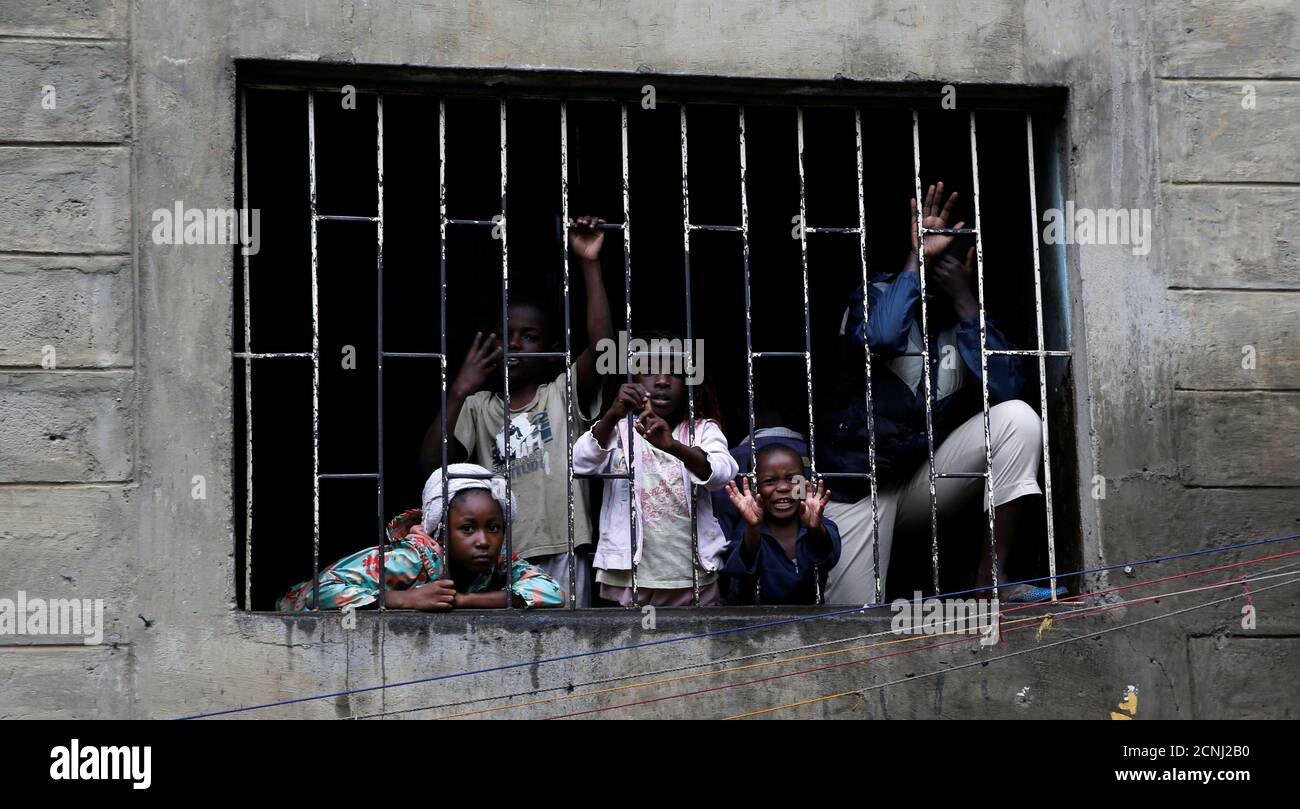Los niños miran a través de una parrilla mientras los trabajadores de rescate buscan a los residentes temidos atrapados en los escombros de un edificio de seis pisos que se derrumbó después de días de fuertes lluvias, en Nairobi, Kenya, 1 de mayo de 2016. REUTERS/Thomas Mukoya IMÁGENES TPX DEL DÍA Foto de stock
