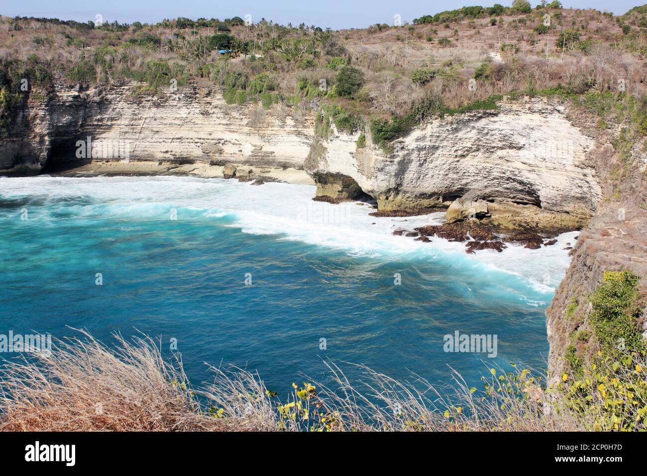 Olas rompiendo en la costa rocosa en el fondo de acantilados empinados, Nusa Penida, Indonesia Foto de stock