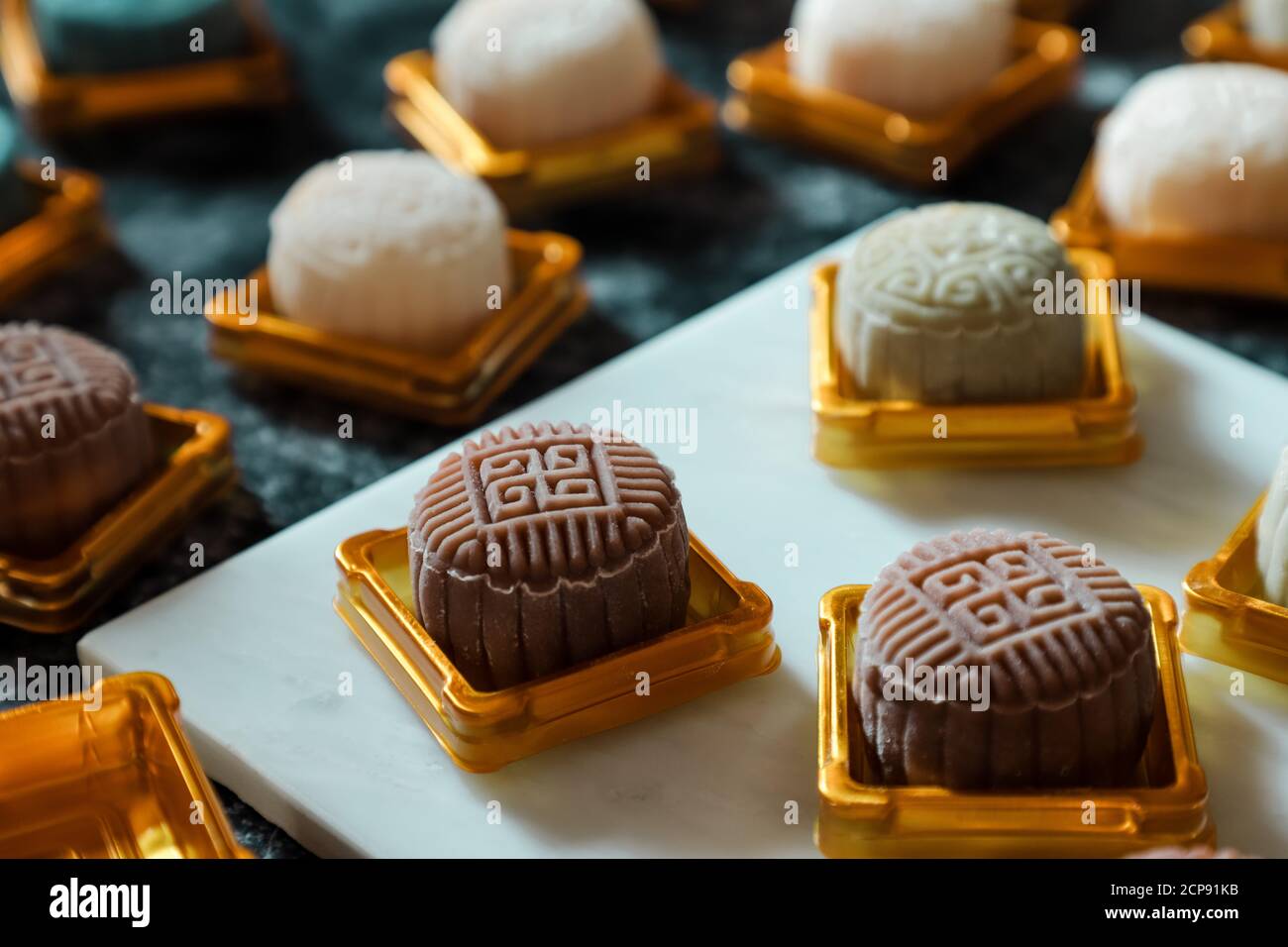 Tortas de luna de piel de nieve en medio del proceso de empaquetado. Colocado en el contenedor plástico dorado; listo para tapar y sellar Foto de stock