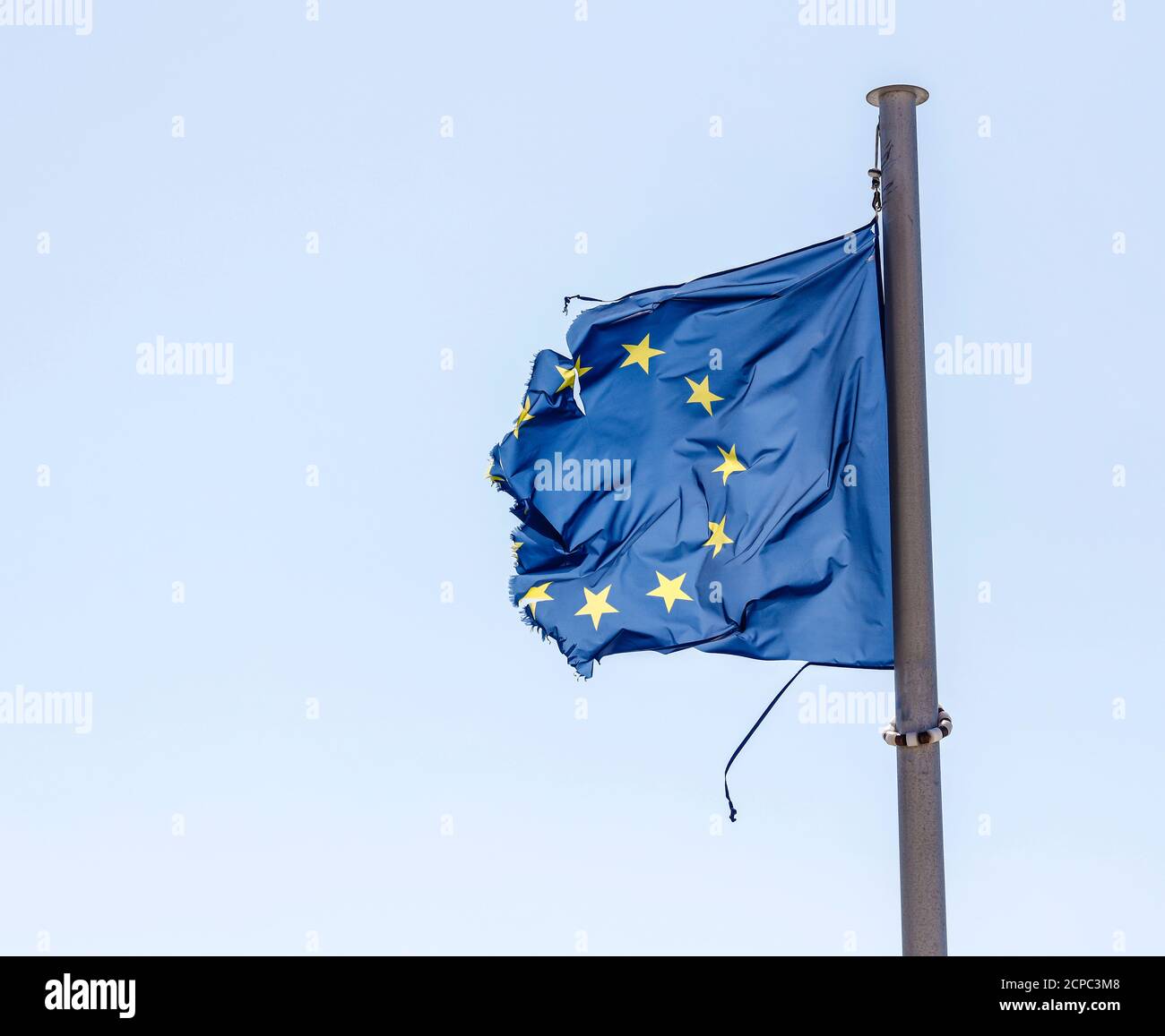 La bandera europea rota flama en el asta de la bandera en el viento, imagen simbólica de EUROPA EN CRISIS. Foto de stock