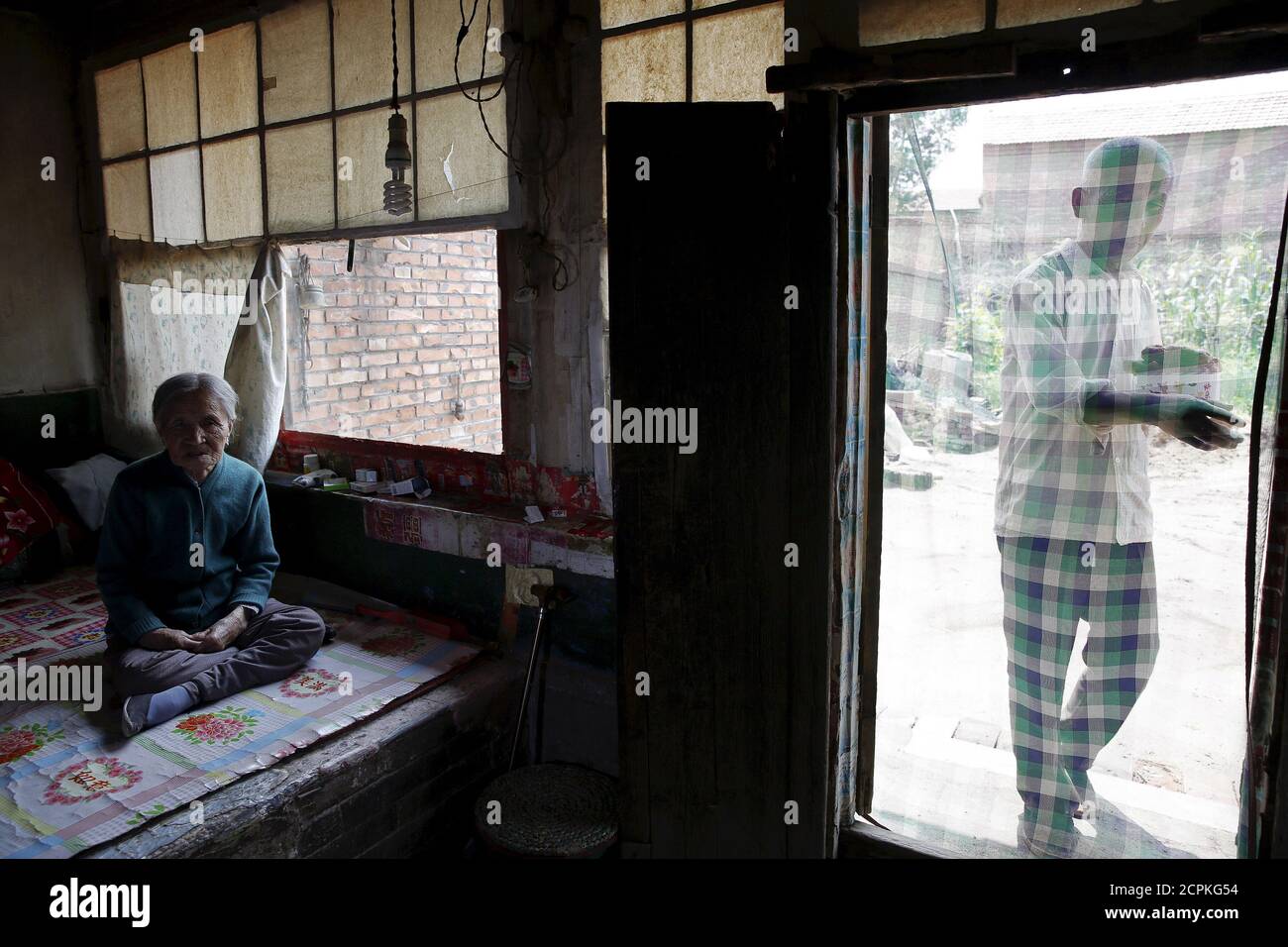 La antigua "mujer de la comodidad" China Zhang Xiantu descansa sobre una cama tradicional de ladrillo mientras su hijo trae su almuerzo en Xiyan Town, Provincia de Shanxi, China, 18 de julio de 2015. œComfort mujer? Es el eufemismo japonés para las mujeres que fueron forzadas a prostituirse y abusadas sexualmente en burdeles militares japoneses antes y durante la Segunda Guerra Mundial. Zhang es la única "mujer de consuelo" sobreviviente de los 16 demandantes en Shanxi que demandó al gobierno japonés en 1995 por secuestrar a niñas y utilizarlas como "mujeres de consuelo" durante la Segunda Guerra Mundial. Según información de la Comisión de Investigación de China Foto de stock