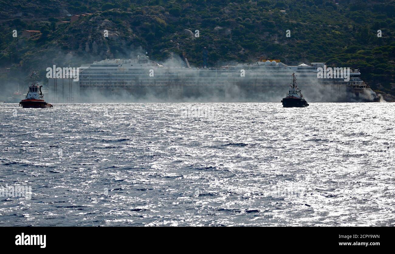 Black smoke comes out from the back of the Costa Concordia cruise liner during its refloat operation at Giglio harbour July 22, 2014. The massive hulk of the Costa Concordia is nearly ready to be towed away from the Italian island where it struck a rock and capsized two-and-a-half years ago, killing 32 people, officials said on Sunday. The 114,500-tonne Concordia has been slowly lifted from the sea floor since Monday, when salvagers began pumping air into 30 large metal boxes, or sponsons, attached around the hull. A convoy of 14 vessels will then tow the Concordia to a port near Genoa, where Foto de stock