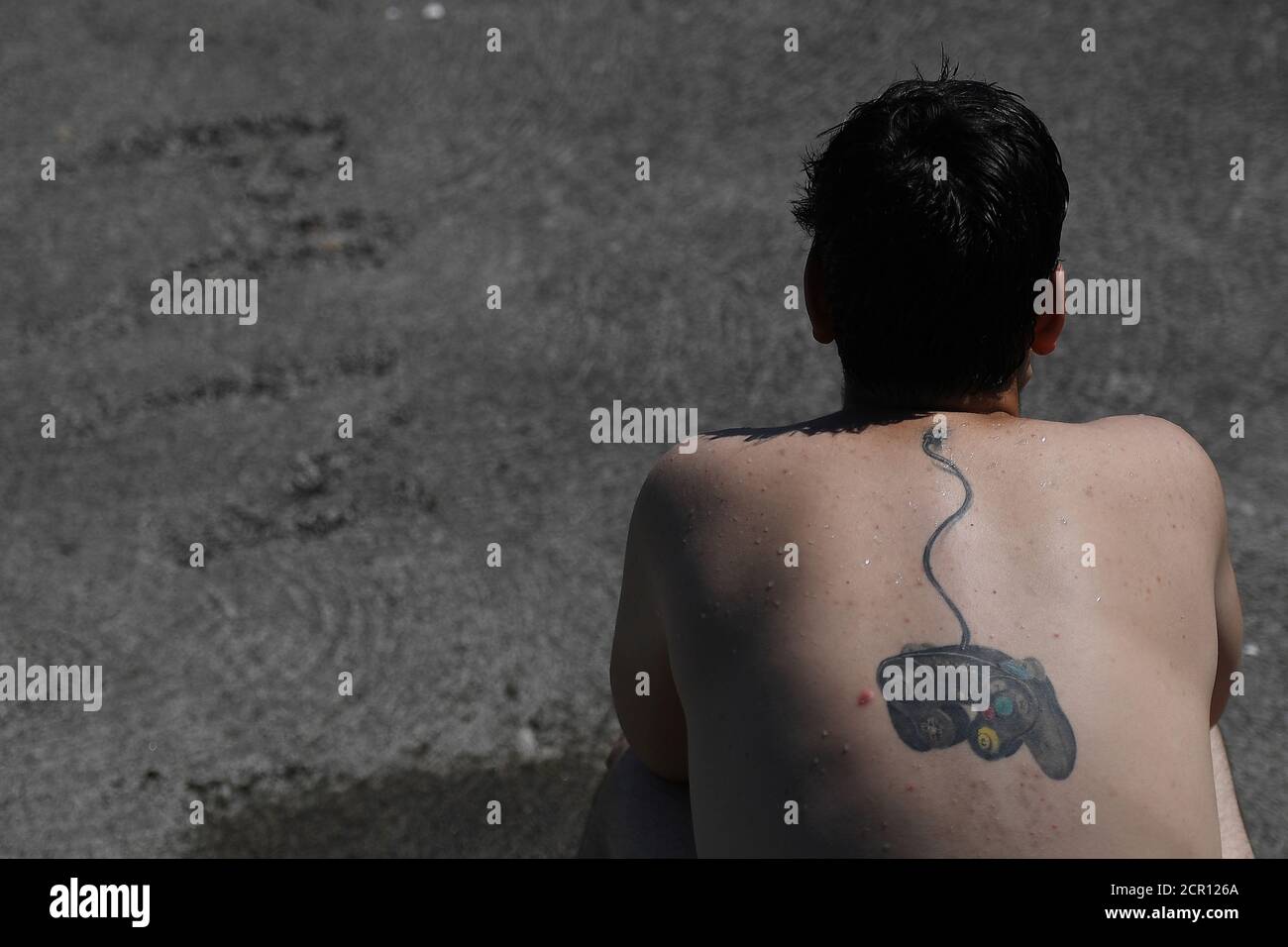 Un hombre se sienta en la playa con su tatuaje de una consola playstation  tapada en su cuello en la playa de Salthill durante el tiempo soleado en  Galway, Irlanda 26 de
