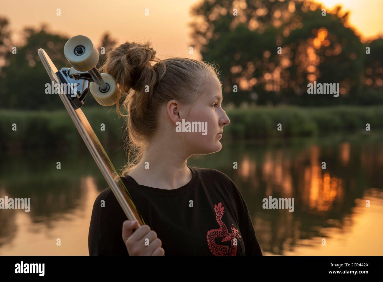 Chica está junto al lago con un longbard al atardecer Foto de stock
