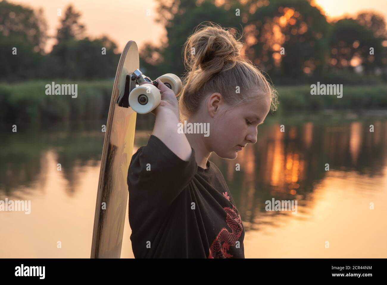Chica está junto al lago con un longbard al atardecer Foto de stock