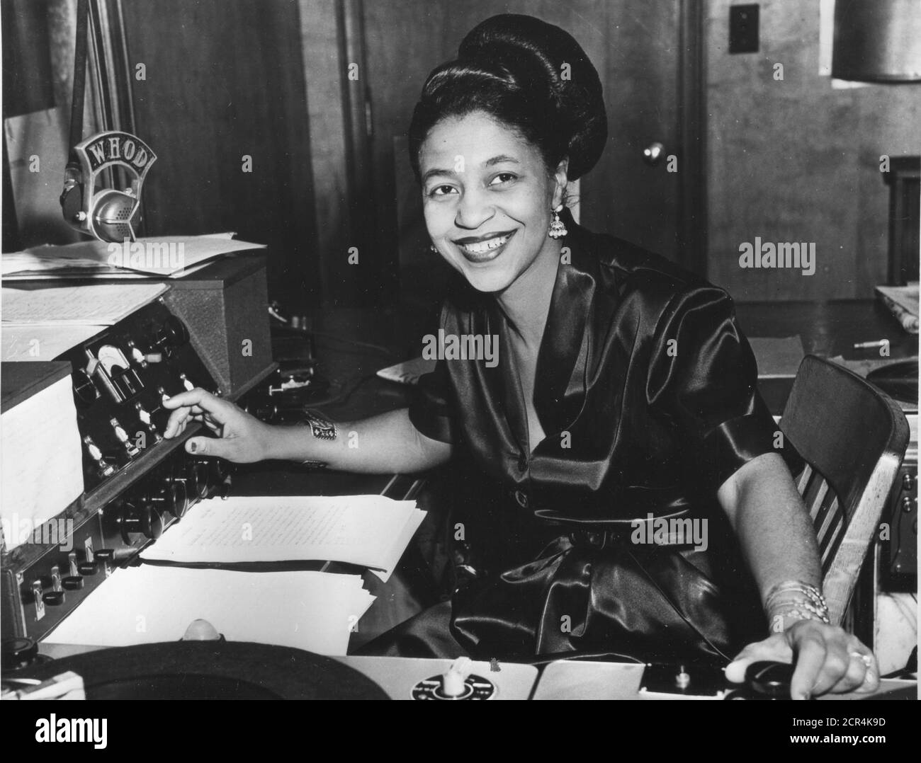 Mary 'Dee' Dudley (1912-1964), ampliamente reconocida como la primera jockey de disco negro femenino con un programa diario, se sienta en los controles en un estudio de estación de radio DONDE ella fue anfitrión de su propio programa, Pittsburgh, PA, 1956. (Foto de RBM Vintage Images) Foto de stock