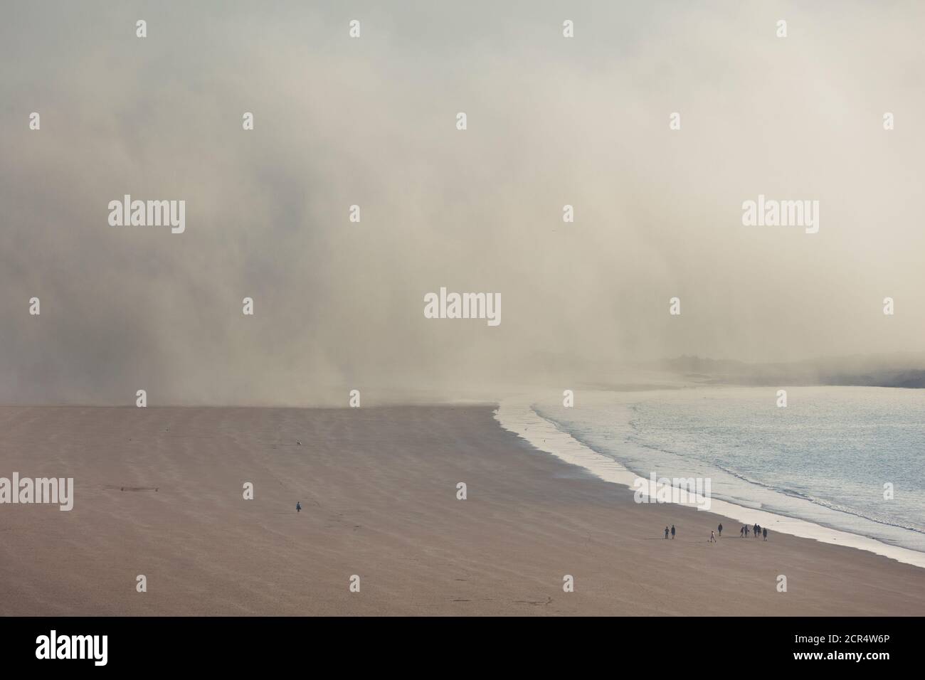 La niebla mareal se mueve sobre la playa en Eruy. Un pequeño grupo de personas (derecha) muestra las proporciones. Erquy, Bretaña, Francia Foto de stock