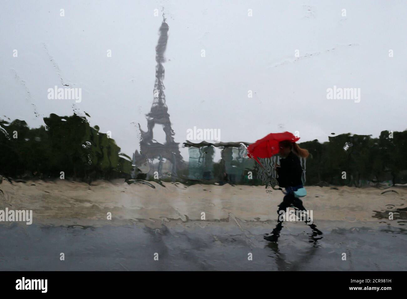 Las gotas de lluvia en la ventana de un coche distorsionan la Torre Eiffel  mientras una mujer se refuta bajo un paraguas rojo durante una ducha de  lluvia en París 13 de