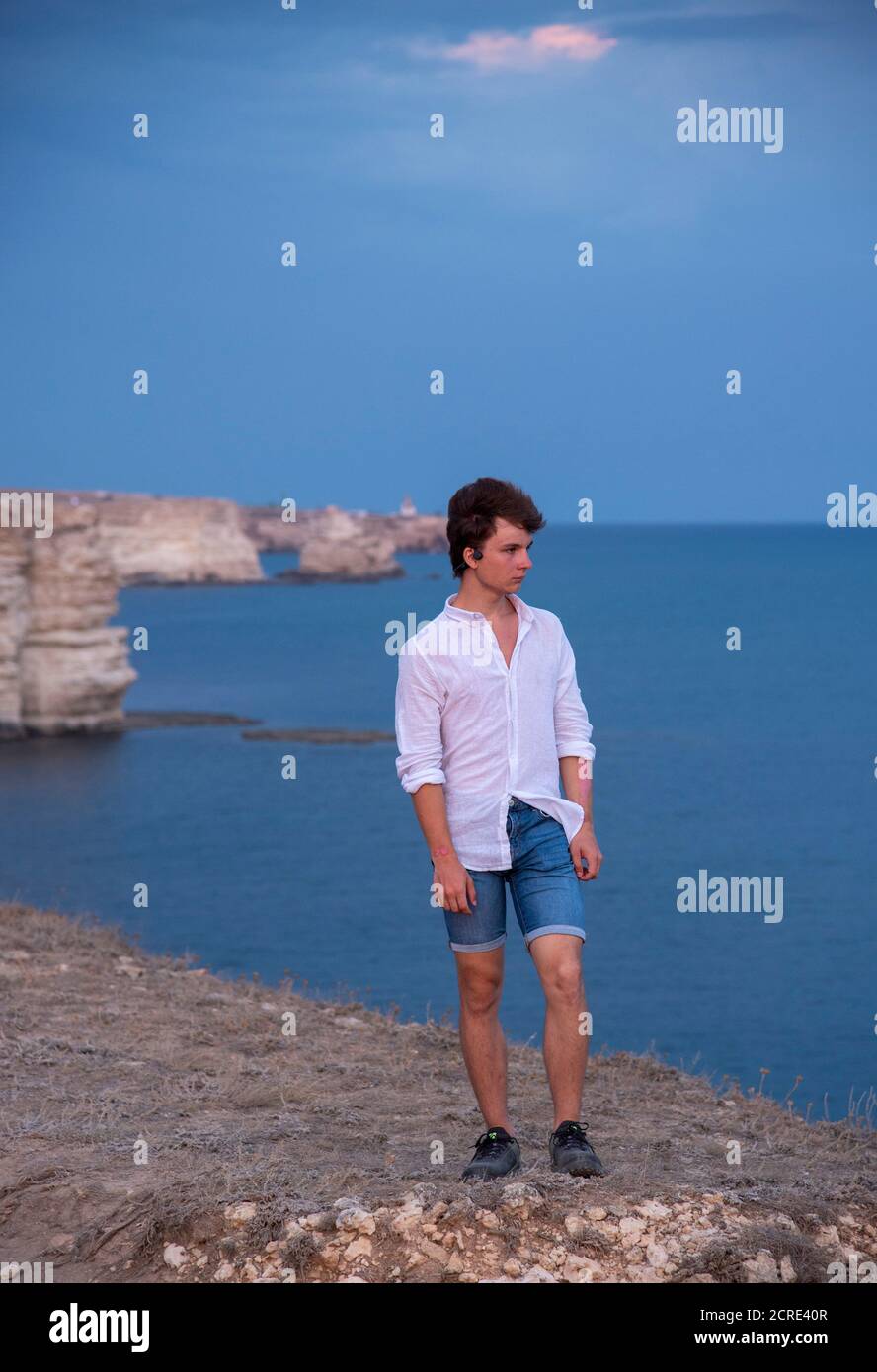Un joven está de pie en una playa rocosa al atardecer. Foto de stock