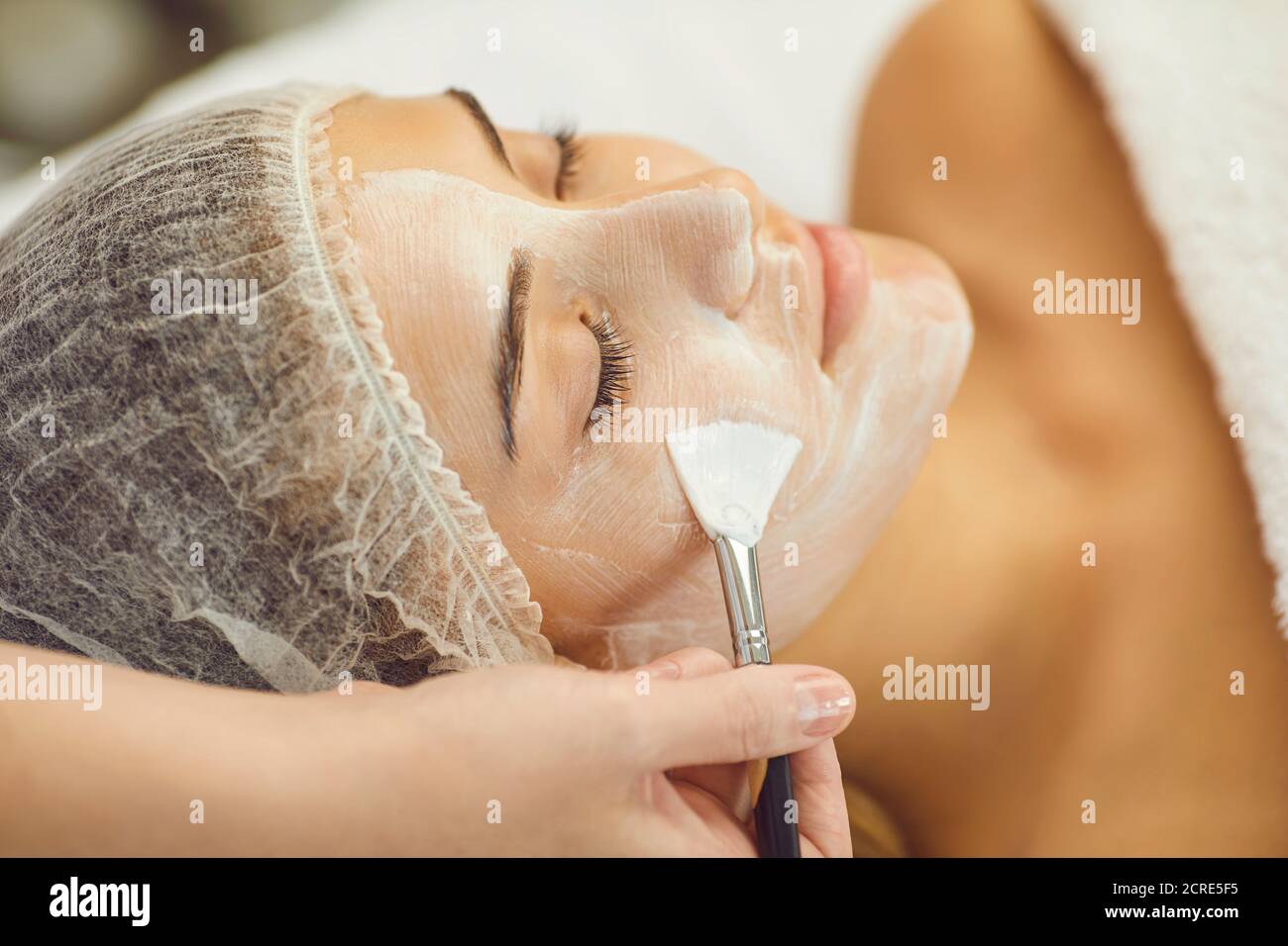 Mujer joven serena que recibe procedimiento de cuidado de la piel de aplicar la máscara hidratante con cepillo de terapeuta Foto de stock