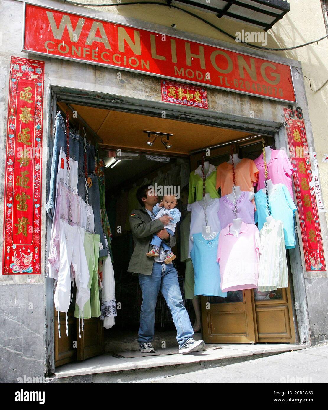 Un hombre que tiene un bebé sale de una tienda mayorista textil China en el centro de Madrid, 17 de mayo de 2005. La Comisión Europea intensificó la presión sobre China para frenar el aumento de las exportaciones textiles, proponiendo conversaciones de emergencia sobre camisetas e hilados de lino que podrían conducir a restricciones rápidas sobre el crecimiento de las importaciones en la UE. REUTERS/Andrea Comas ACO/JK Foto de stock