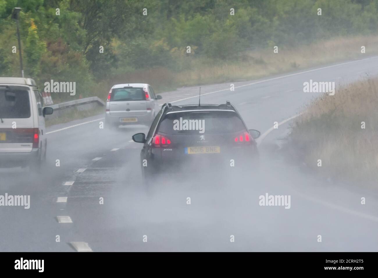 Conductores conduciendo coches en una carretera de dos carriles durante fuertes lluvias con poca visibilidad en Inglaterra, Reino Unido. Mal tiempo y carretera húmeda y peligrosa mientras llueve. Foto de stock