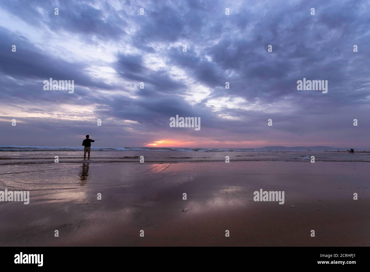 Un joven pescando en el mar abierto a lo largo de la costa del Océano Atlántico en Costa da Caparica en Lisboa, Portugal. Un chico atractivo que sostiene la pesca ro Foto de stock