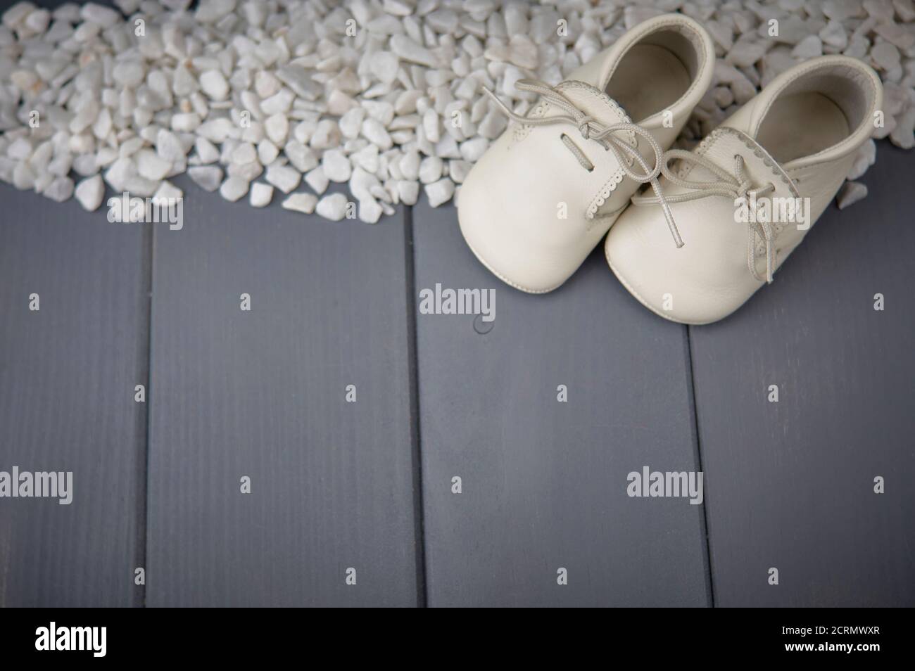 Vista superior de un par de zapatos blancos recién nacidos con cordones atados, sobre el fondo de piedras blancas y madera gris Foto de stock