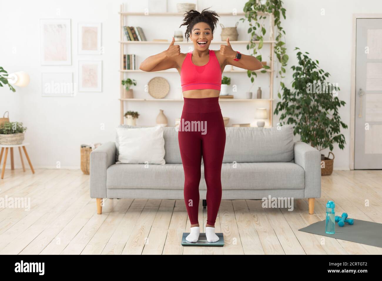 Black Fitness Lady Gestuing Thumbs-Up de pie en escalas en casa Foto de stock