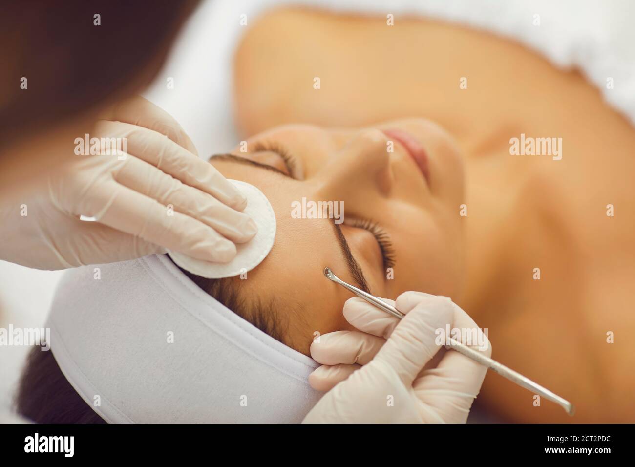 Un esteticista hace la limpieza mecánica de la cara de una mujer en una clínica cosmética. Cosmetólogo que hace la limpieza de la piel para la mujer joven en el salón de belleza Foto de stock