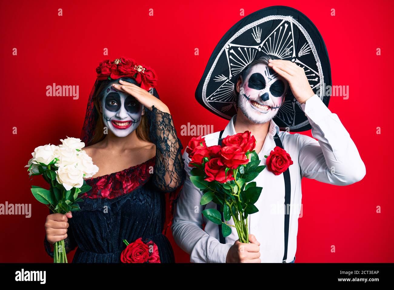 Pareja que lleva el día del traje muerto sosteniendo flores estresadas y frustradas con la mano en la cabeza, cara sorprendida y enojada Foto de stock