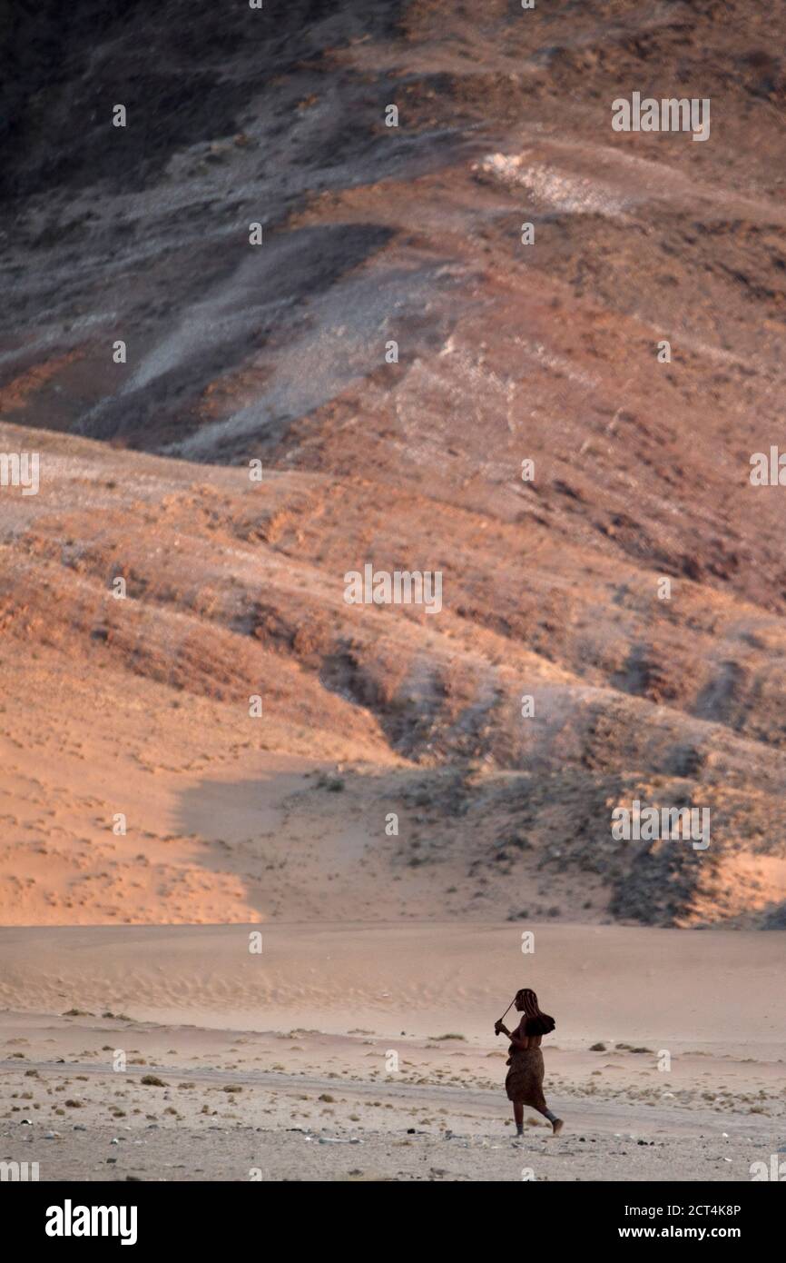 Una mujer Himba camina por la árida región que rodea su hogar en la región de Kunene de Namibia. Foto de stock
