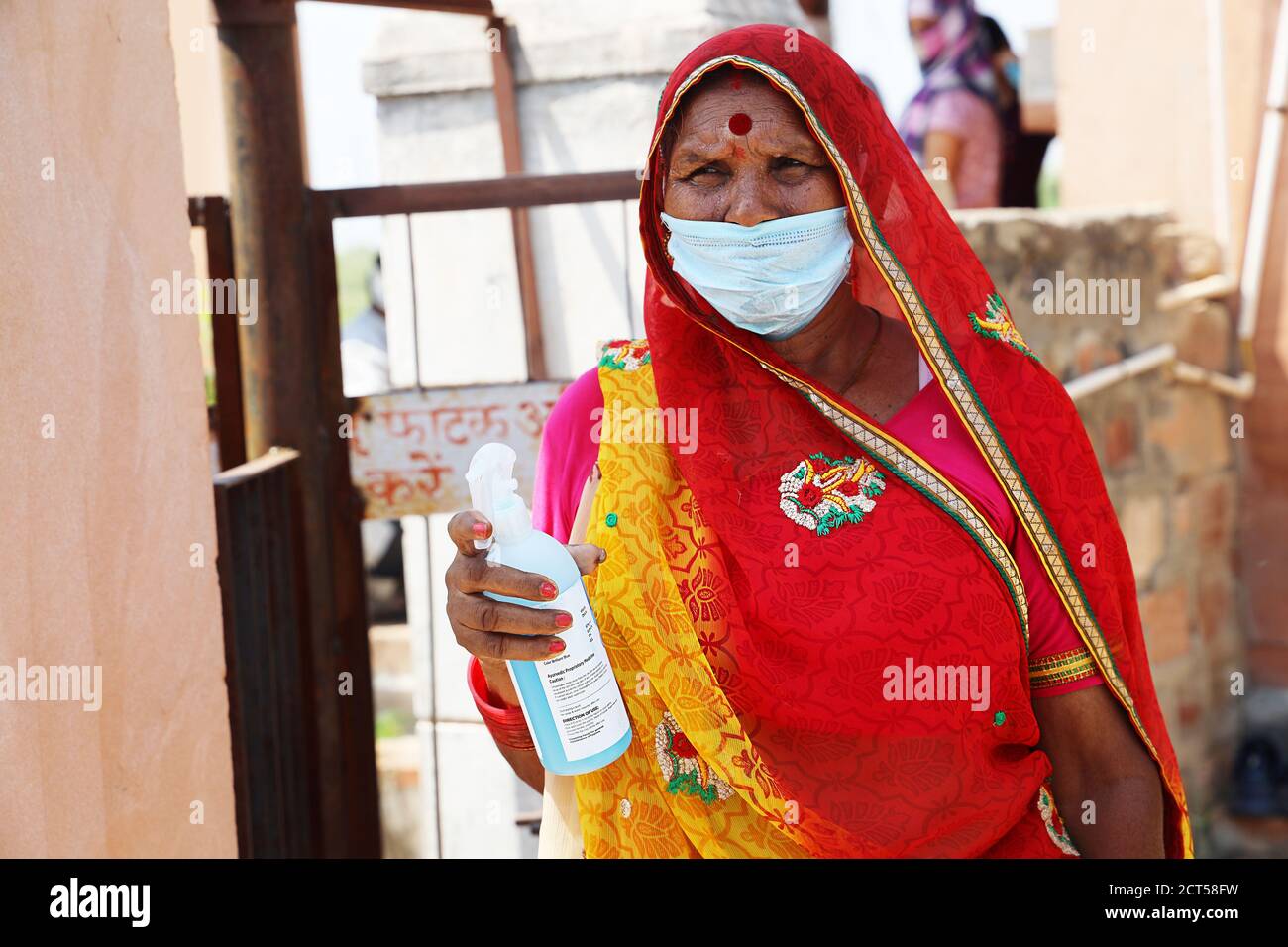 Jodhpur, Rajasthan, India, septiembre de 13,2020: Mujer anciana tradicional sosteniendo botella de higienizador usando máscara de pie al aire libre, trabajador social lucha con c Foto de stock