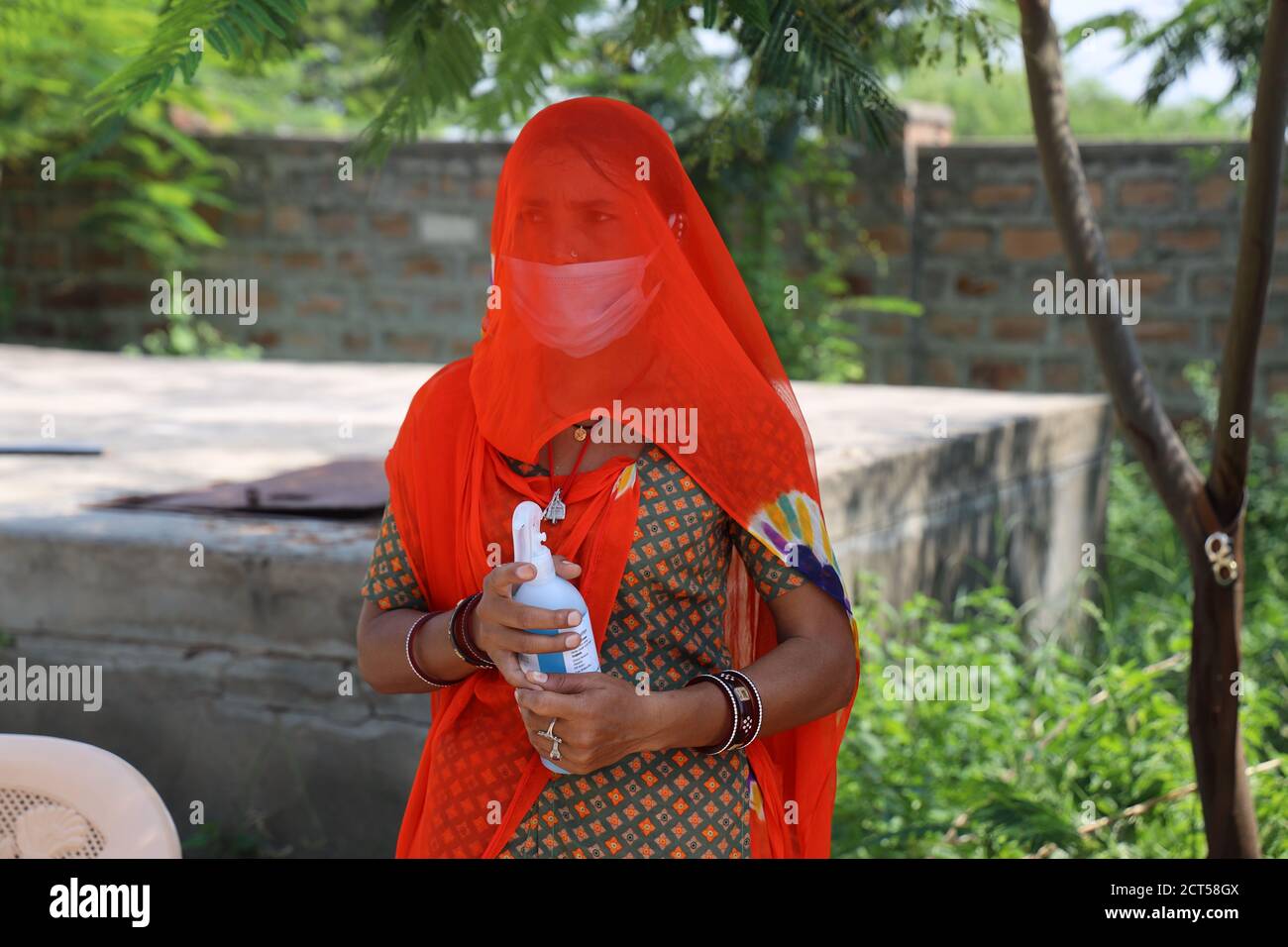 Jodhpur, Rajasthan, India, septiembre de 13,2020: Mujer tradicional en velo sosteniendo botella de higienizador usando máscara de pie al aire libre, trabajador social lucha wi Foto de stock