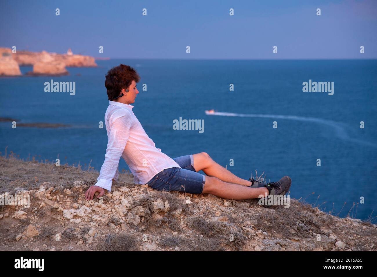 Un joven está de pie en una playa rocosa al atardecer. Foto de stock