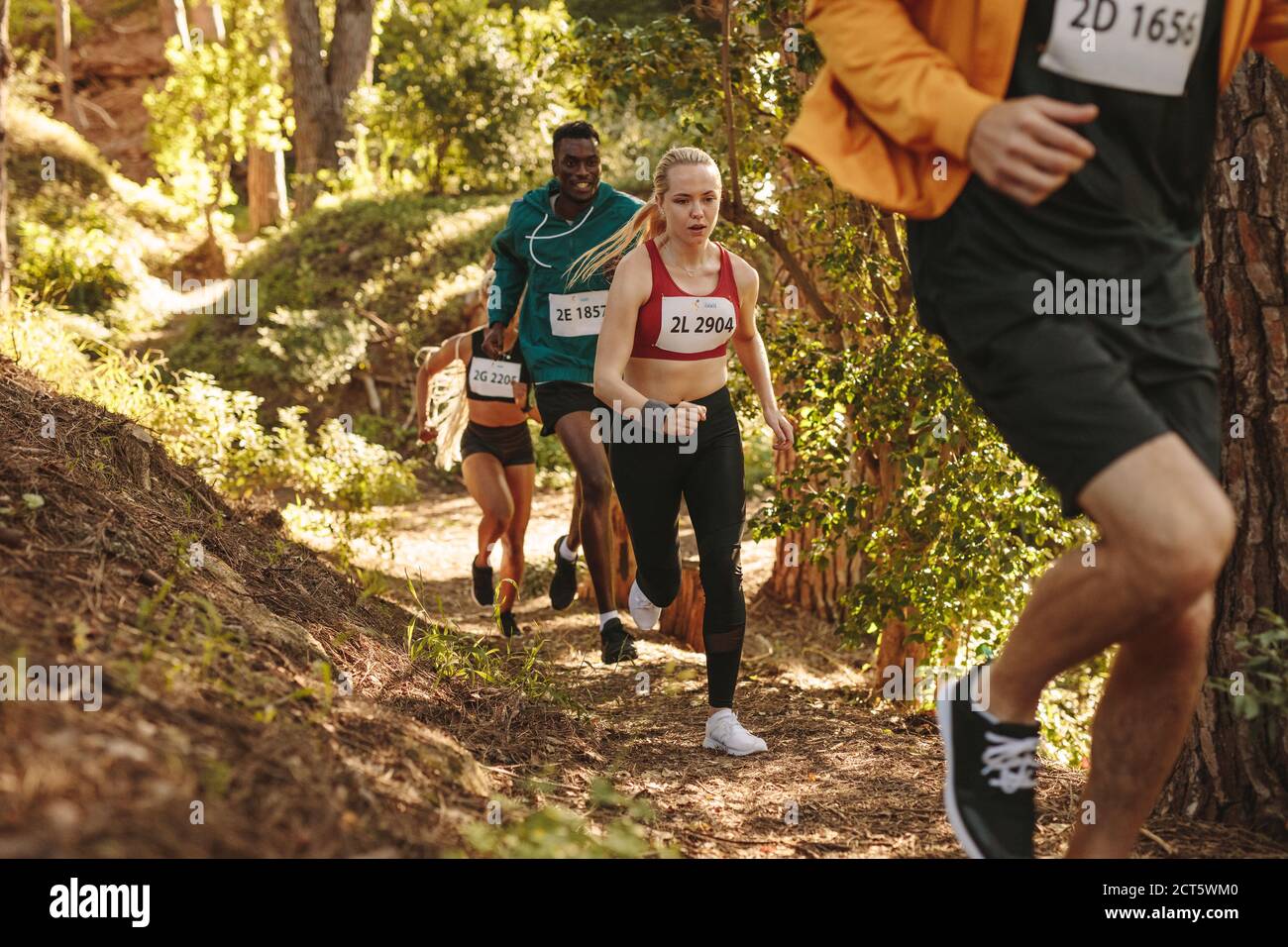 Grupo de atletas corredores correr camino cuesta arriba. Hombres y mujeres corriendo una carrera de maratón. Foto de stock