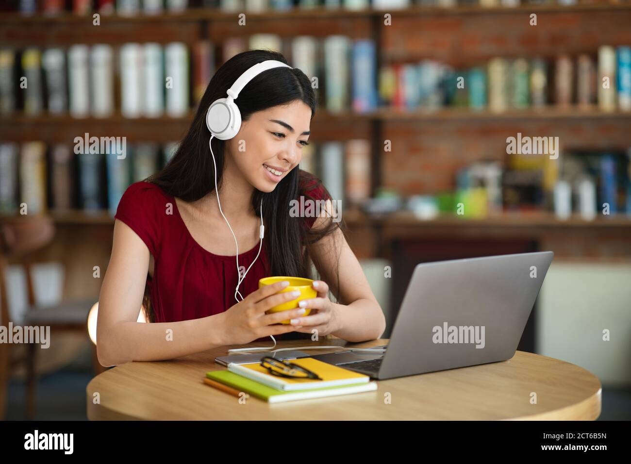 Sonriente mujer asiática viendo Webinar con portátil y auriculares en Café Foto de stock