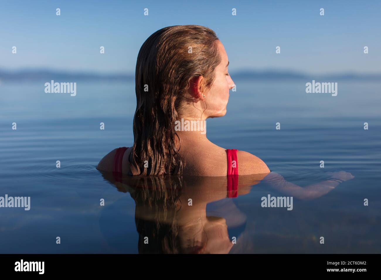 Una adolescente nadando en un lago, cabeza y hombros sobre el agua del lago al amanecer, los ojos cerrados Foto de stock