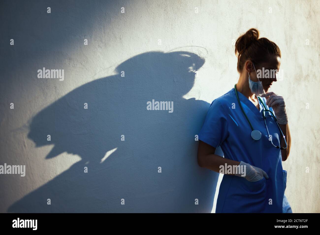 pandemia de coronavirus. mujer médica moderna estresada en peelings con estetoscopio, máscara médica y guantes de goma al aire libre en la ciudad cerca de la pared. Foto de stock