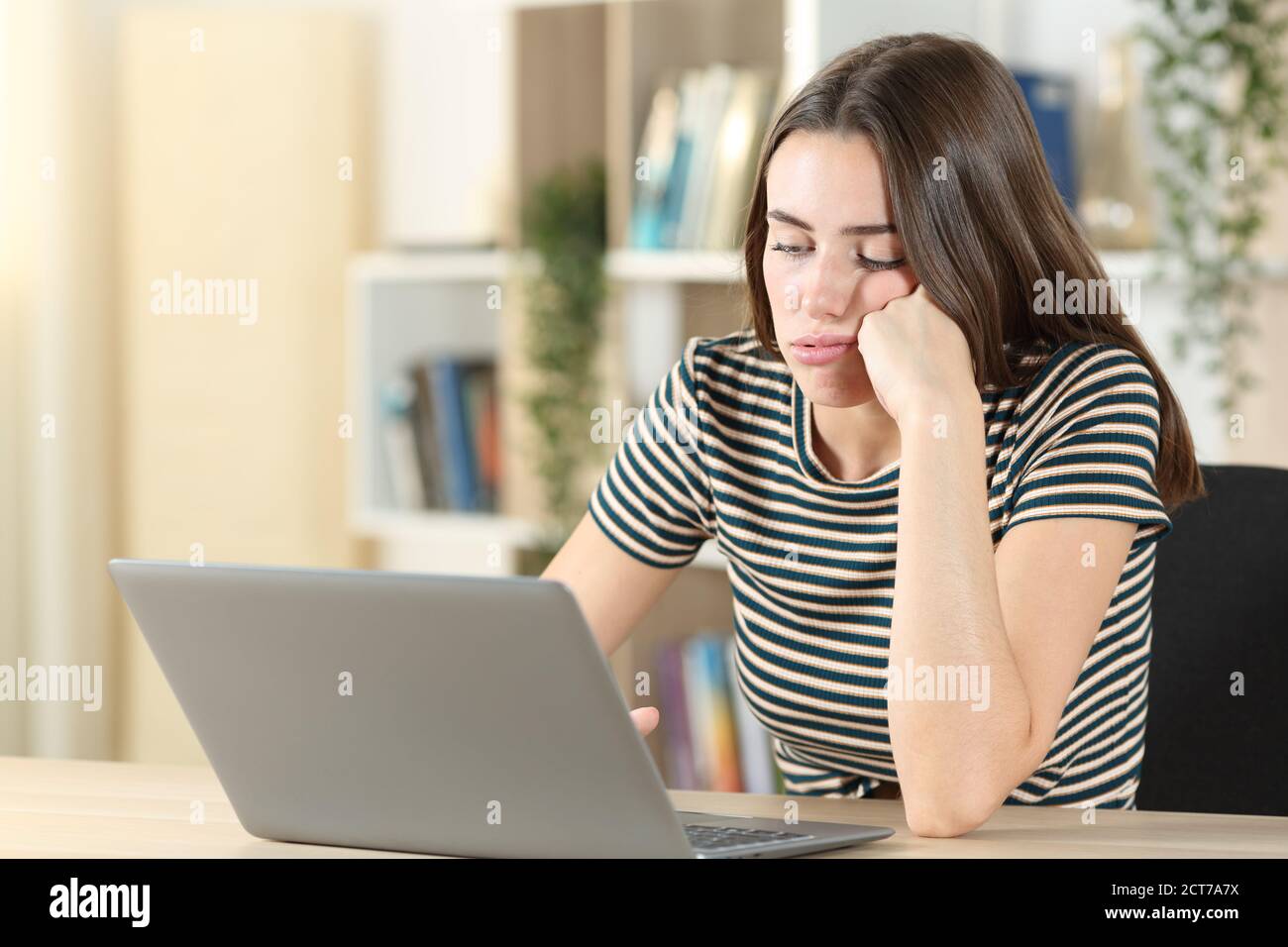 Adolescente aburrido usando un portátil perdiendo tiempo sentado en un escritorio en casa Foto de stock