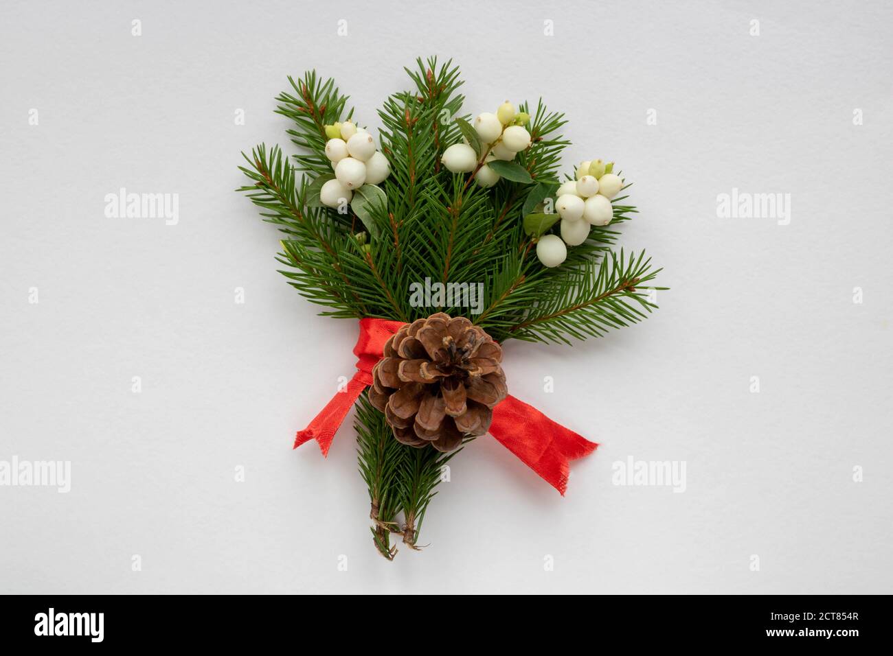 Ramo de Navidad con ramas de abeto, arco rojo, piña y bayas blancas de  madera de perrito sobre un fondo blanco . Tarjeta de Navidad. El tema de  las vacaciones de invierno