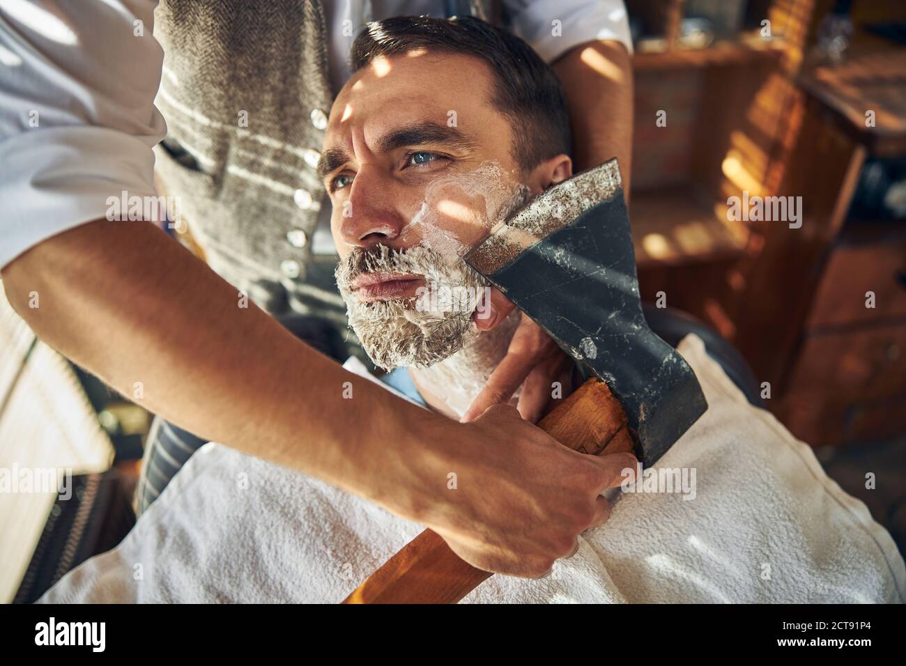 Un hombre joven guapo que está siendo afeitado con un hacha Foto de stock