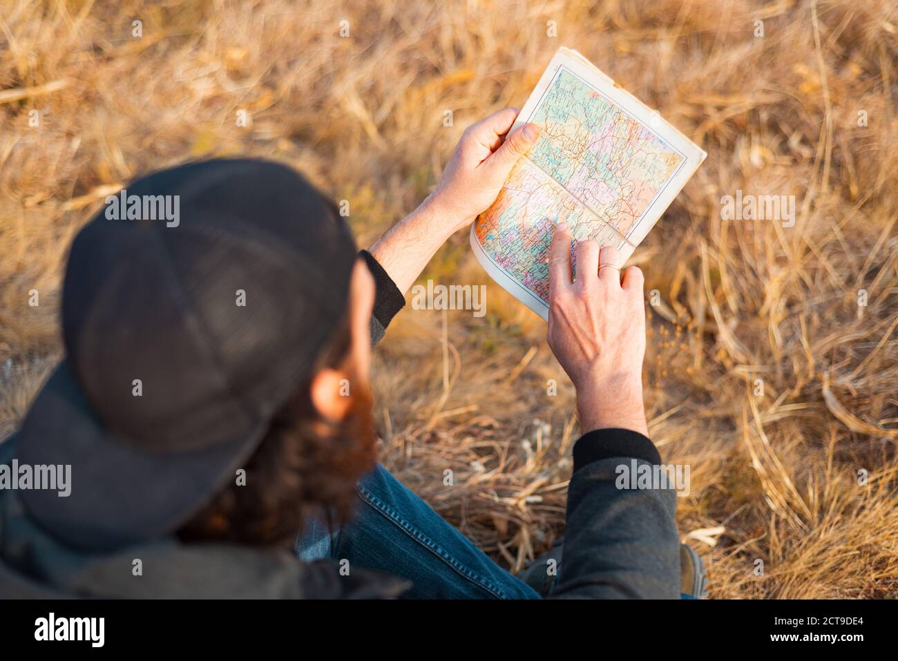 Un joven está sentado en el campo y mirando en un mapa . Foto de stock