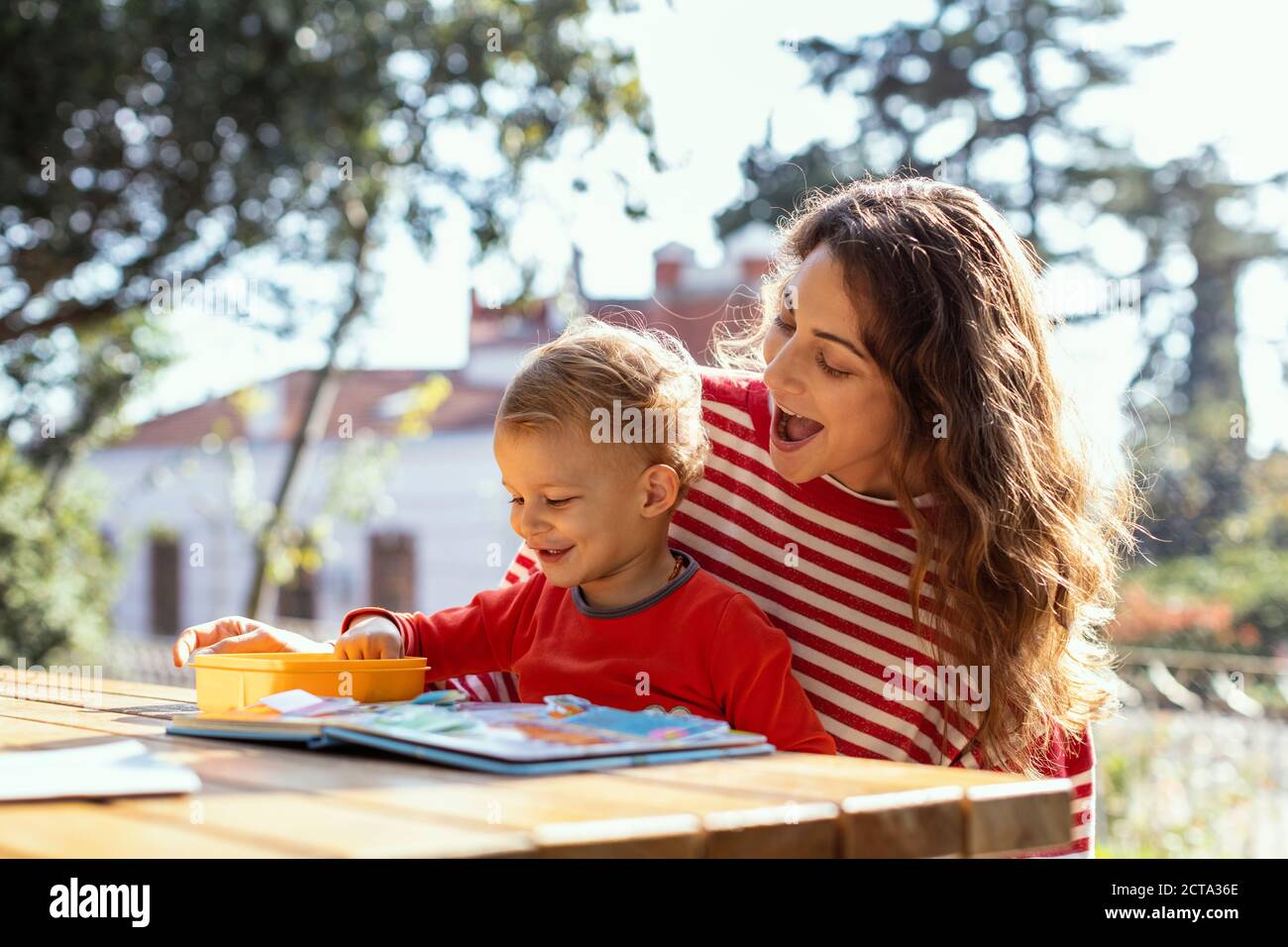 Feliz Madre y niño leyendo Lift-the-flap niños Libro y comer Aperitivos en el jardín Foto de stock