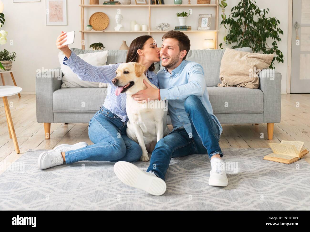 Pareja joven tomando selfie con su perro en la sala de estar Foto de stock