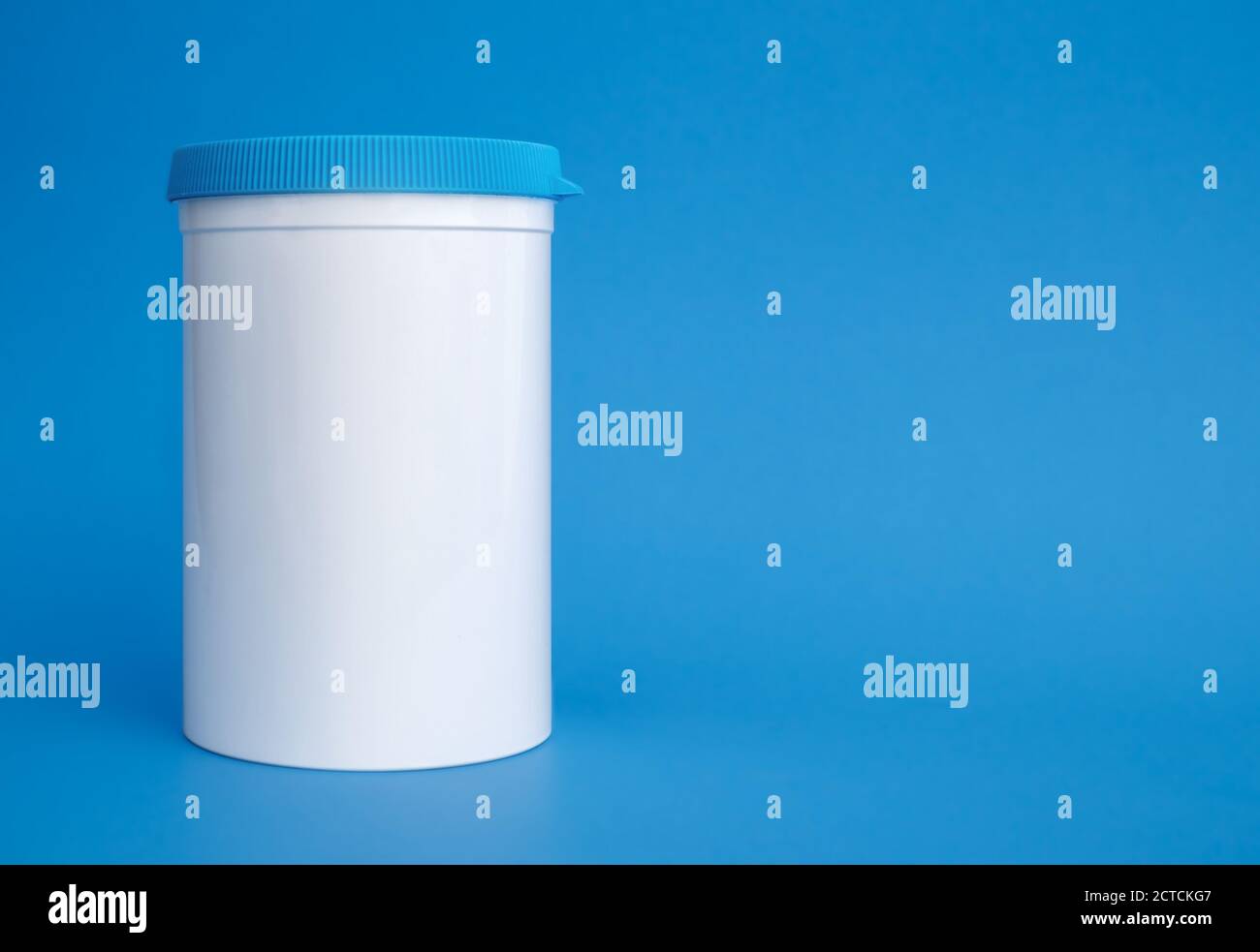 Dispensador de pastillas puede o tarro. Contenedor de plástico blanco grande con tapón de rosca azul, reutilizable. Se utiliza para dispensar y almacenar suplementos y medicamentos. Foto de stock