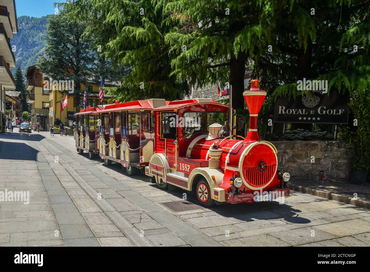 Un pequeño tren turístico estacionado frente al Grand Hotel Royal e Golf de 5 estrellas en el centro de la ciudad de montaña en verano, Courmayeur, Aosta, Italia Foto de stock