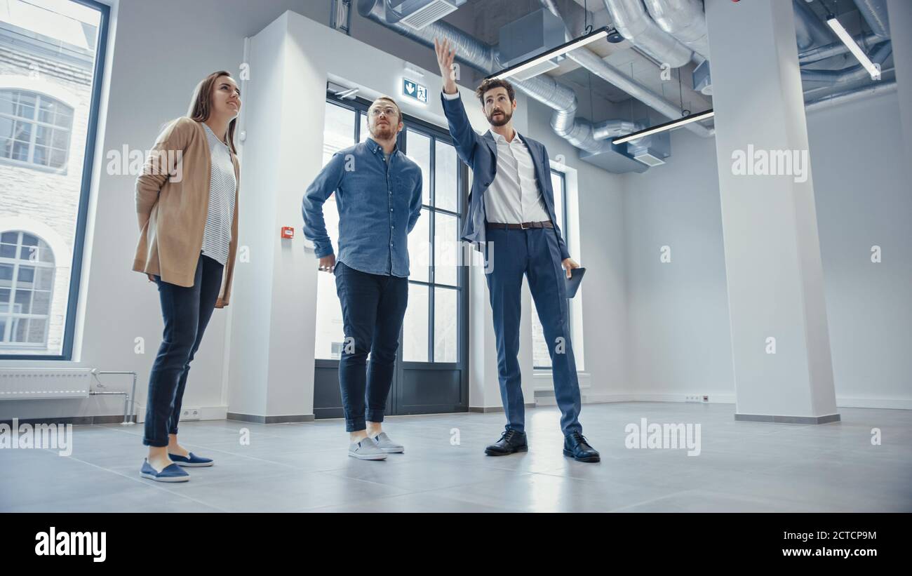 Agente inmobiliario mostrando un nuevo espacio de oficina vacío a jóvenes hombres y mujeres Hipsters. Los empresarios se reúnen con el Broker con una tableta y discutir el Foto de stock