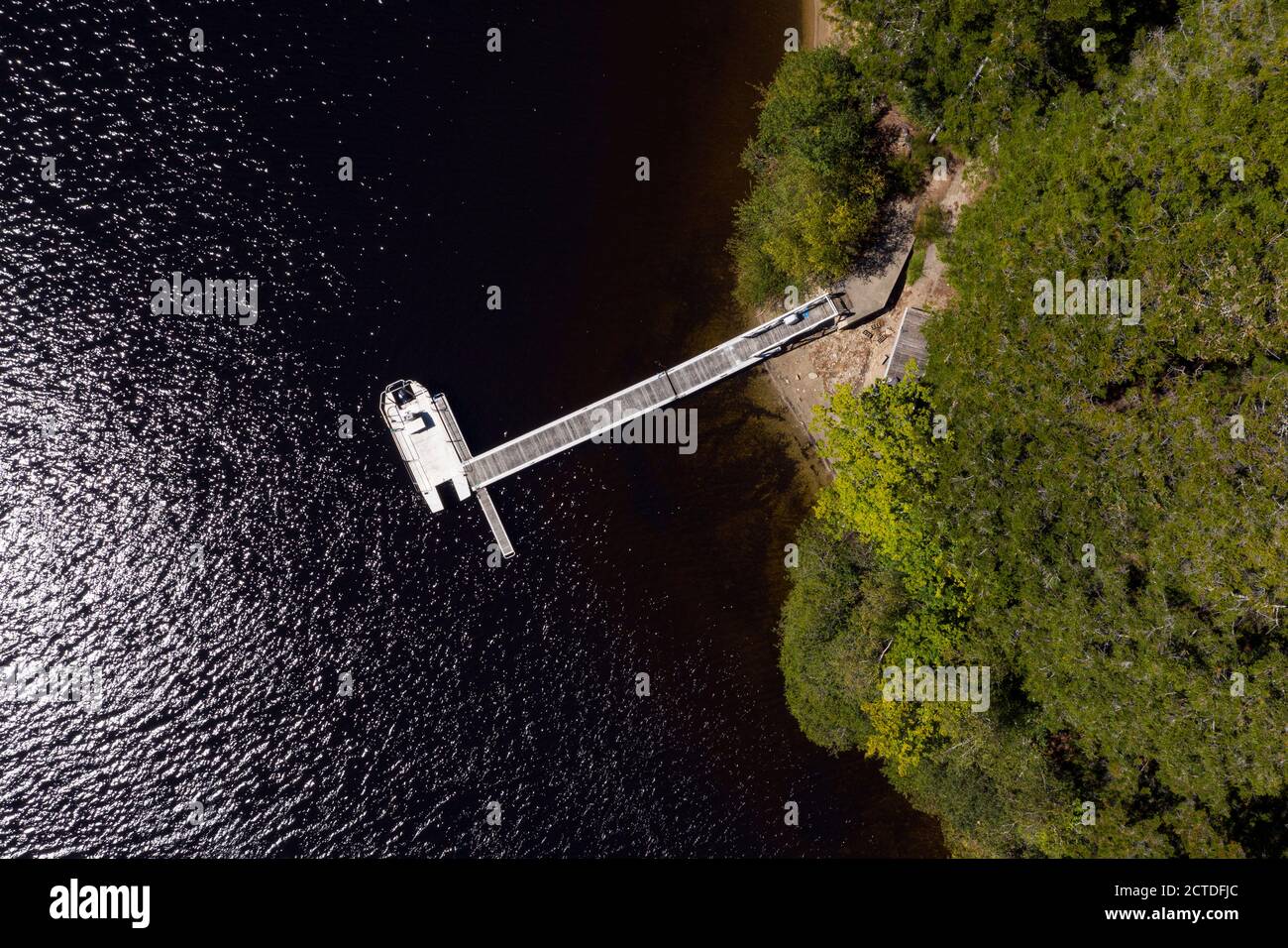 Vista aérea superior foto de muelle privado con un barco a motor en la orilla de la remota isla cubierta de bosque. Foto de stock
