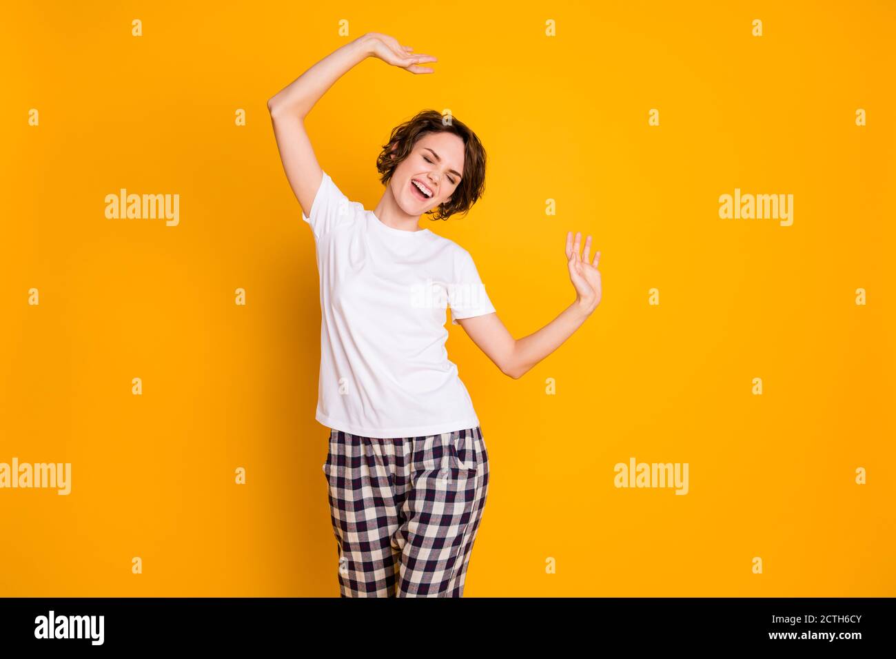 Retrato de alegre chica cándita tienen fiesta de pijamas levantar las manos siéntase regocijarse intente bailar lleve pijama aislado sobre colores vivos antecedentes Foto de stock