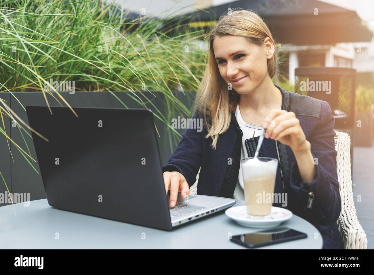 mujer joven bebiendo café latte en la terraza del café al aire libre y trabajando con el ordenador portátil Foto de stock