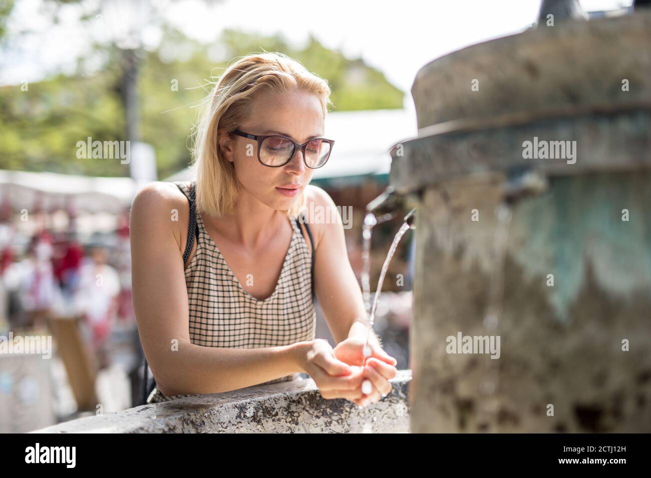Mujer cucasiana joven sedienta de agua potable de la ciudad pública fuente en un caluroso día de verano Foto de stock