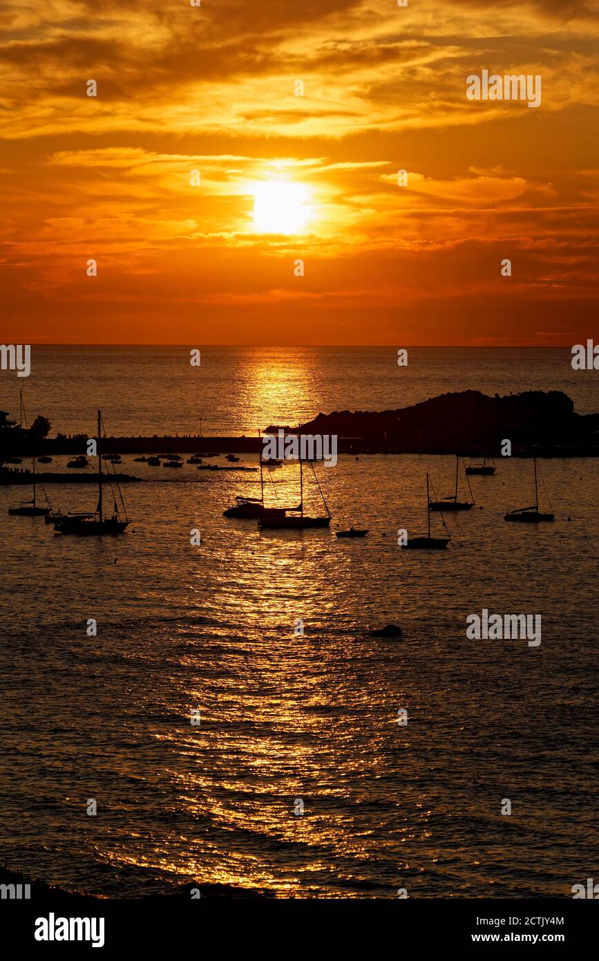 Francia, Haute-Corse, Lile-Rousse, Silhouettes de veleros en frente de la pequeña isla mediterránea a la puesta de sol moody Foto de stock